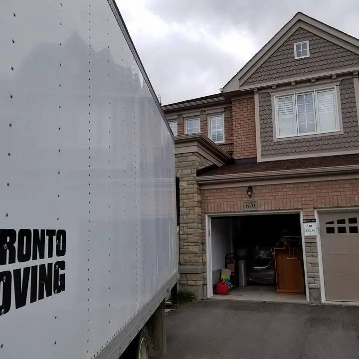 A Toronto moving truck parked in front of a suburban home with a garage open and furniture inside, s